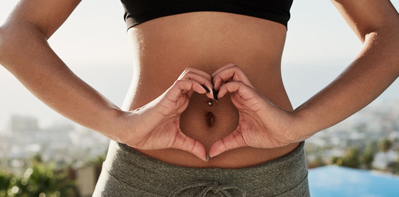 A woman is making a heart shape with her hands on her stomach