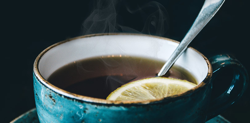 A hot cup of tea with a sliced lemon and spoon in it