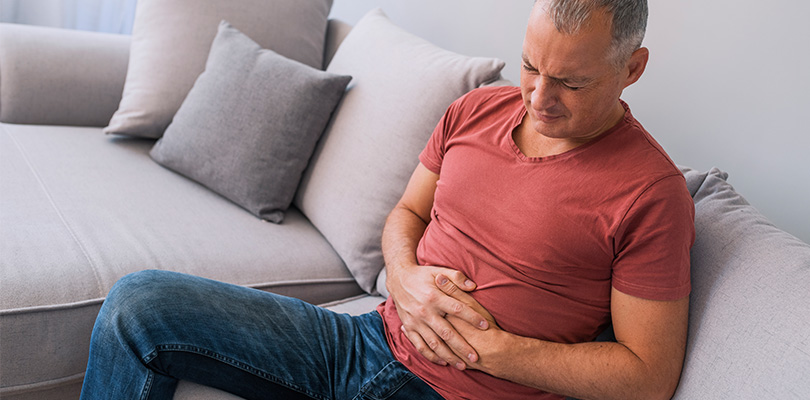 Man sitting on couch holding his stomach in pain